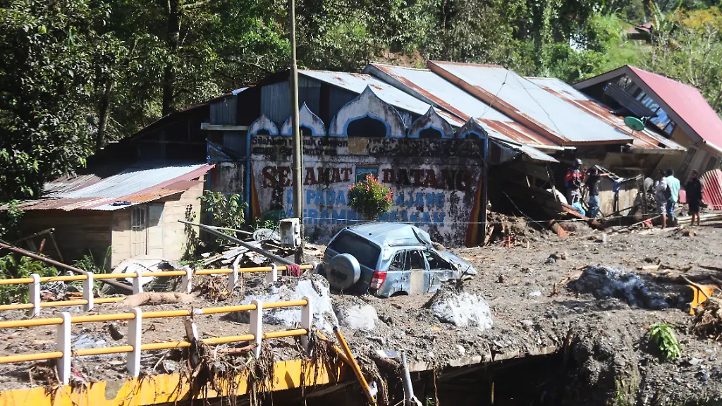 Das-Wrack-eines-Autos-liegt-mitten-auf-einer-Strasse-waehrend-Menschen-die-Schaeden-nach-der-Sturzflut-in-Padang-Panjang-begutachten