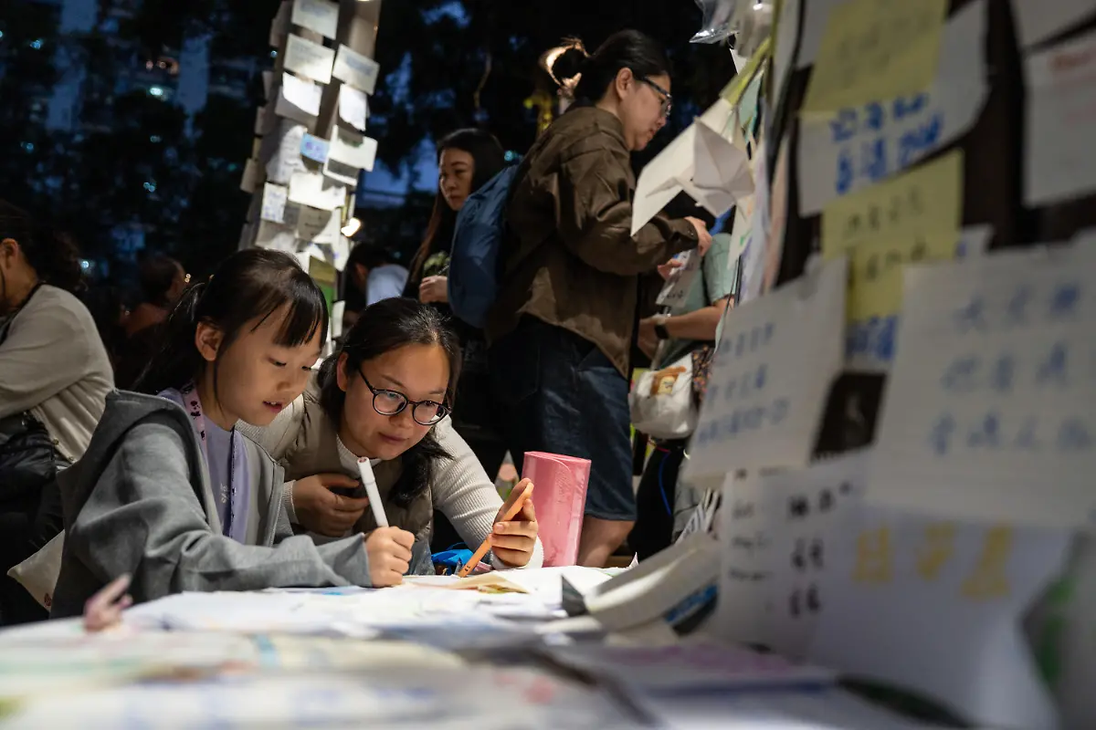 A-girl-writing-a-note-at-a-makeshift-memorial-near-Wang-Fuk-Court-housing-complex-in-Tai-Po-following-a-deadly-fire-on-November-30-2025-in-Hong-Kong