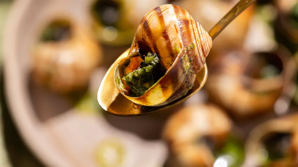 Close-up-image-of-baked-escargot-garnished-with-parsley-and-butter-served-in-a-circular-dish-with-a-fork