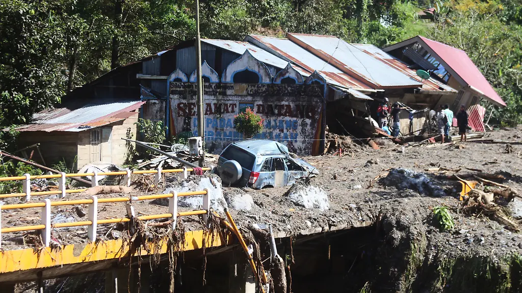 29-11-2025-Indonesien-Padang-Panjang-Das-Wrack-eines-Autos-liegt-mitten-auf-einer-Strasse-waehrend-Menschen-die-Schaeden-nach-der-Sturzflut-in-Padang-Panjang-begutachten