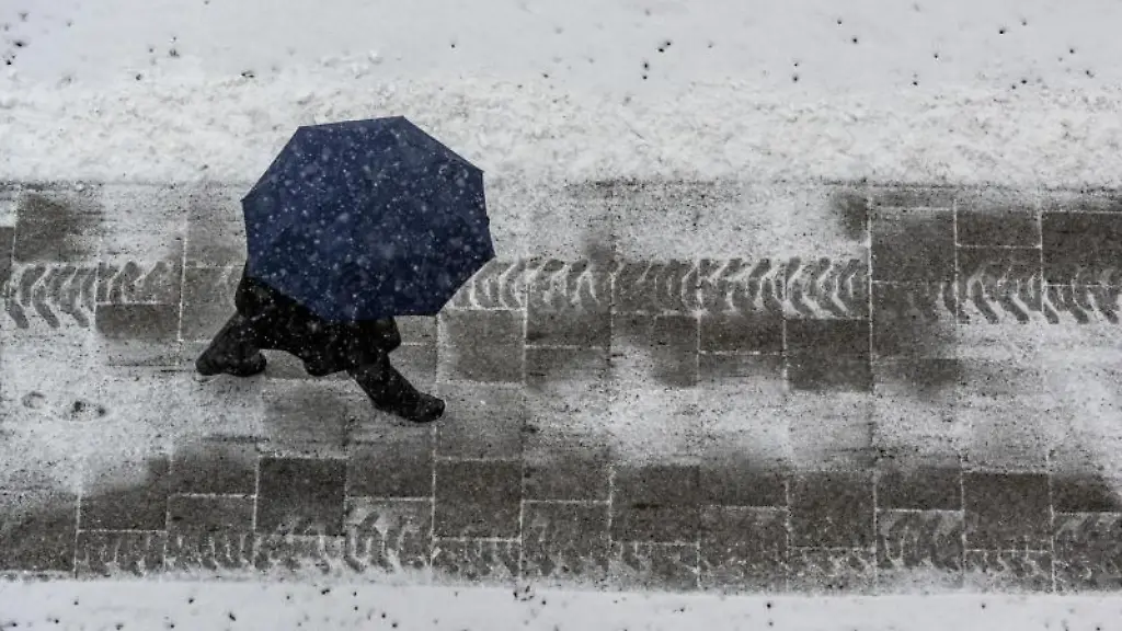 Ein-Fussgaenger-mit-Regenschirm-ist-auf-einer-mit-Schnee-bedeckten-Strasse-unterwegs