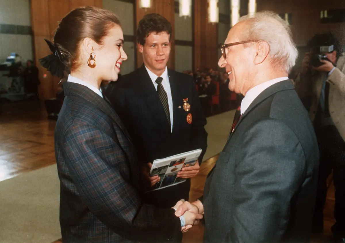 Der-DDR-Staatsratsvorsitzende-Erich-Honecker-schuettelt-bei-einer-Ehrung-von-olympischen-Medaillengewinnern-am-25-04-1988-in-Ostberlin-Eiskunstlauf-Olympiasiegerin-Katarina-Witt-die-Hand-Katarina-Witt-hatte-in-Calgary-ihren-Olympiasieg-von-1984-wiederholt-Frank-Peter-Roetsch-M-Biathlon-Doppel-Olympiasieger-in-Calgary-ueber-10-und-20-km-schaut-zu