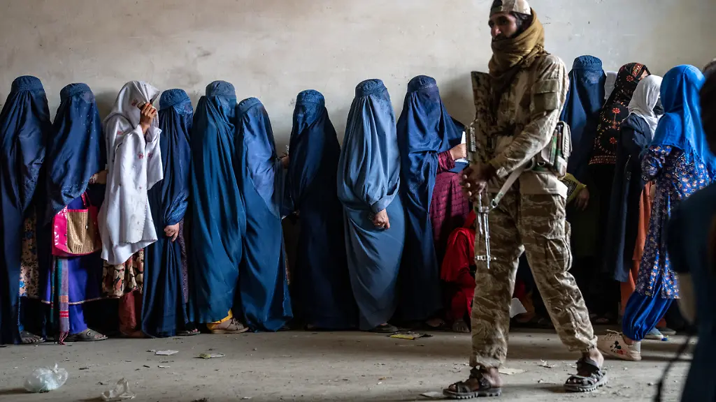 A-Taliban-fighter-stands-guard-as-women-wait-to-receive-food-rations-distributed-by-a-humanitarian-aid-group-in-Kabul-Afghanistan-Tuesday-May-23-2023