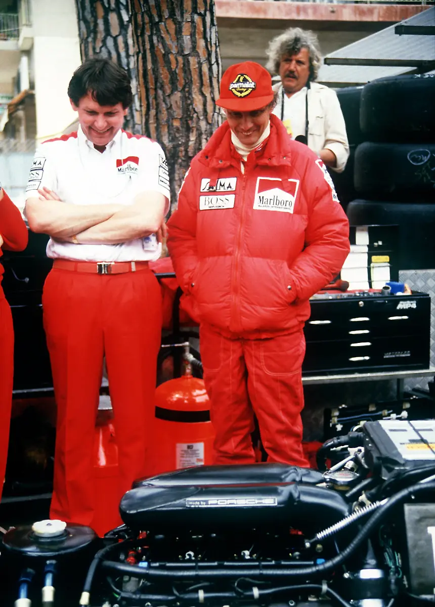 Der-oesterreichische-Formel-1-Rennfahrer-Niki-Lauda-r-schaut-sich-laechelnd-zusammen-mit-einem-Techniker-vor-dem-Start-zum-Grossen-Preis-von-Monaco-in-Monte-Carlo-einen-TAG-Turbomotor-Porsche-an-Aufnahme-von-1984