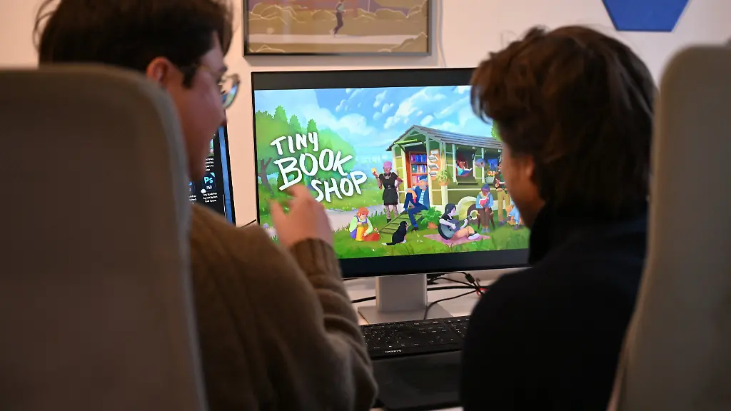PRODUKTION-02-12-2025-NA-Koeln-Die-Computerspiele-Entwickler-David-Zapfe-Wildemann-l-und-Raven-Rusch-von-dem-Koelner-Independent-Gamingstudio-Neoludic-sitzen-in-ihrem-Buero-vor-einem-Bildschirm-auf-dem-die-Startseite-des-Spiels-Tiny-Bookshop-zu-sehen-ist-Das-Spiel-hat-sich-beim-Deutschen-Entwicklerpreis-in-drei-Kategorien-durchgesetzt-darunter-in-der-Kategorie-Bestes-Deutsches-Spiel