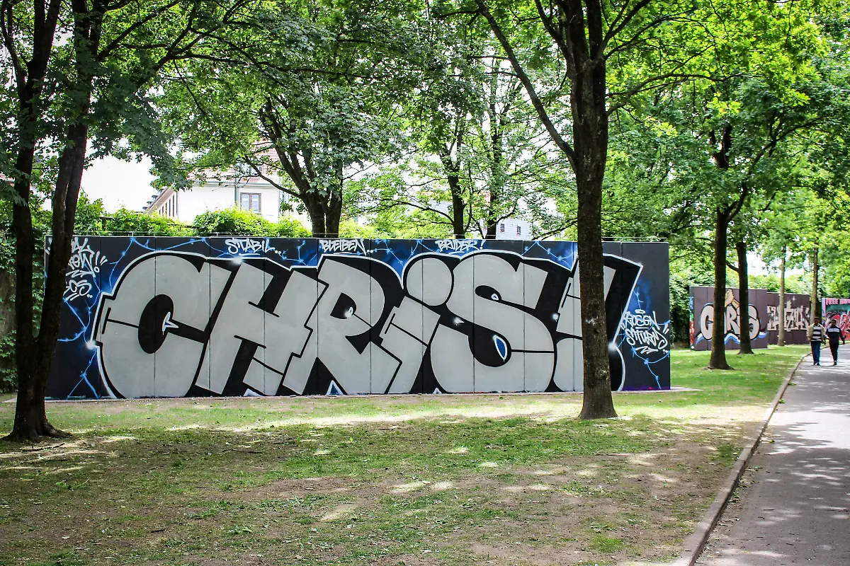 Ein-Graffiti-mit-dem-Namen-Chris-in-einer-Gruenanlage-in-Bielefeld-zum-Gedenken-an-einen-jungen-Mann-der-bei-einer-Messerattacke-vor-der-Cutie-Bar-am-Sonntag-dem-18-05-2025-zusammen-mit-drei-anderen-jungen-Menschen-mutmasslich-von-einem-35-jaehrigen-Syrer-schwer-verletzt-wurde-Foto-vom-23-05-2025-Knapp-eine-Woche-nach-dem-Messerangriff-in-Bielefeld-hat-eine-Gruppierung-aus-dem-rechten-Spektrum-fuer-Samstag-einen-Aufmarsch-mit-Mahnwache-in-der-Stadt-angekuendigt-Dazu-wuerden-200-Teilnehmer-erwartet-teilte-die-Polizei-Bielefeld-am-Freitag-mit-Die-angemeldete-Versammlung-soll-vor-dem-Tatort-der-Tanzbar-Cuties-stattfinden-Das-Motto-der-rechtsgerichteten-Kundgebung-lautet-Anteilnahme-fuer-die-Opfer-vom-18-05-2025-und-Remigration-Ein-Bielefelder-Buendnis-rief-zu-einer-Gegendemonstration-unter-dem-Motto-Gegen-Hass-und-Hetze-in-Bielefeld-auf-Dazu-sind-laut-Polizei-500-Teilnehmerinnen-und-Teilnehmer-angemeldet-Man-sei-mit-verstaerkten-Kraeften-im-Einsatz-und-gehe-von-einem-friedlichen-Verlauf-der-Versammlungen-aus-erklaerte-das-Polizeipraesidium-Bielefeld-Siehe-epd-Meldung-vom-23-05