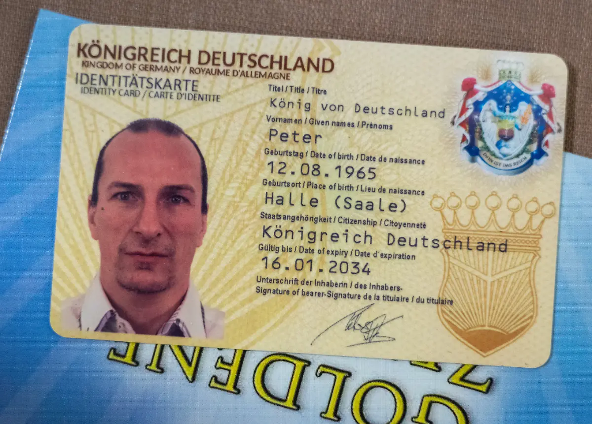 Die-Identitaetskarte-des-Reichsbuerger-Aktivisten-Peter-Fitzek-liegt-im-Landgericht-Dessau-auf-seinem-Platz-Fitzek-der-sich-selbst-auch-Koenig-von-Deutschland-nennt-war-vor-rund-einem-Jahr-wegen-vorsaetzlicher-Koerperverletzung-und-Beleidigung-schuldig-gesprochen-und-zu-acht-Monaten-Freiheitsstrafe-ohne-Bewaehrung-verurteilt-worden-Weil-Berufung-eingelegt-wurde-wird-der-Fall-nun-noch-einmal-verhandelt-Die-Bundesanwaltschaft-hat-am-13-05-2025-vier-mutmassliche-Raedelsfuehrer-der-verbotenen-Reichsbuerger-Gruppe-Koenigreich-Deutschland-festnehmen-lassen-darunter-Gruender-Peter-Fitzek
