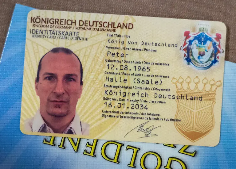Die-Identitaetskarte-des-Reichsbuerger-Aktivisten-Peter-Fitzek-liegt-im-Landgericht-Dessau-auf-seinem-Platz-Fitzek-der-sich-selbst-auch-Koenig-von-Deutschland-nennt-war-vor-rund-einem-Jahr-wegen-vorsaetzlicher-Koerperverletzung-und-Beleidigung-schuldig-gesprochen-und-zu-acht-Monaten-Freiheitsstrafe-ohne-Bewaehrung-verurteilt-worden-Weil-Berufung-eingelegt-wurde-wird-der-Fall-nun-noch-einmal-verhandelt-Die-Bundesanwaltschaft-hat-am-13-05-2025-vier-mutmassliche-Raedelsfuehrer-der-verbotenen-Reichsbuerger-Gruppe-Koenigreich-Deutschland-festnehmen-lassen-darunter-Gruender-Peter-Fitzek