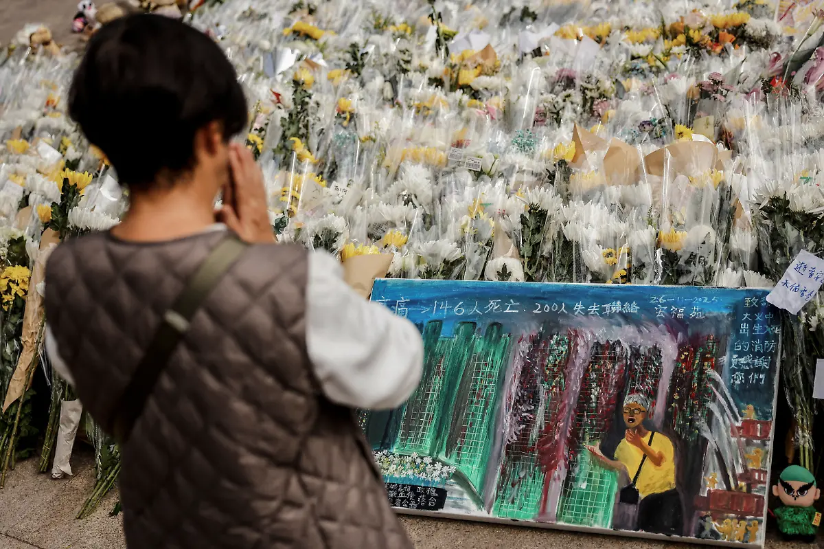 A-woman-prays-as-a-painting-depicting-a-photograph-taken-by-Reuters-photographer-Tyrone-Siu-sits-at-a-makeshift-flower-memorial-near-the-Wang-Fuk-Court-housing-complex-after-the-deadly-fire-in-Tai-Po-Hong-Kong-China-December-1-2025-REUTERS-Maxim-Shemetov-SEARCH-HONG-KONG-FIRE-PICTURE-FOR-THIS-STORY-SEARCH-WIDER-IMAGE-FOR-ALL-STORIES