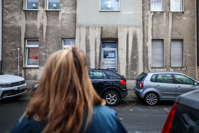 Eine-Frau-steht-vor-einem-Mehrfamilienhaus-In-einem-Mehrfamilienhaus-in-Bochum-ist-ein-zwoelfjaehriges-Maedchen-bei-einem-Polizeieinsatz-durch-Schuesse-aus-einer-Dienstwaffe-lebensgefaehrlich-verletzt-worden