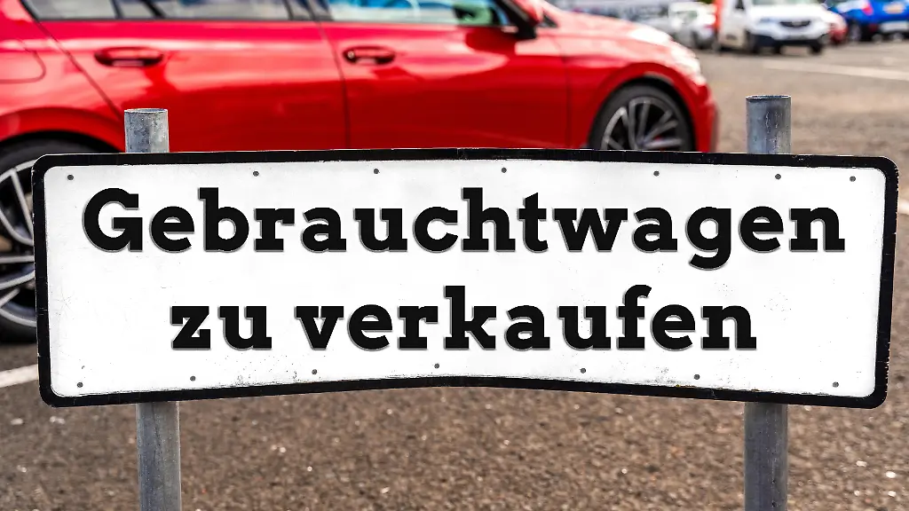 FOTOMONTAGE-Ein-Schild-mit-der-Aufschrift-Gebrauchtwagen-zu-verkaufen-steht-auf-einem-Parkplatz-vor-einem-roten-Auto