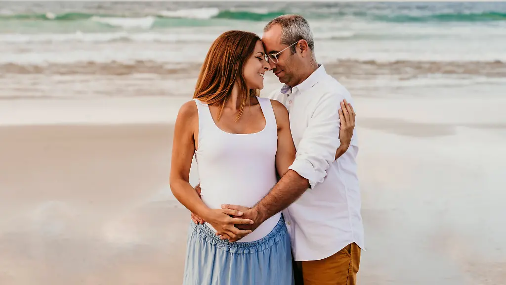 Smiling-man-taking-care-and-embracing-pregnant-woman-at-beach-model-released-Symbolfoto-EBBF08963