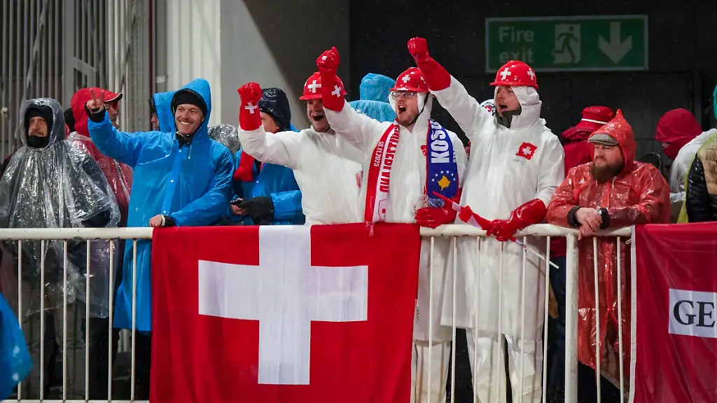 Fussball-WM-Qualifikation-2025-26-10-Spieltag-Kosovo-vs-Schweiz-Fadil-Vokrri-Stadion-Pristina-Pristina-Kosovo-Europa-Schweizer-Fans-im-Regen-weisse-Schutzanzuege-rote-Helme-mit-Kreuz-Schweiz-Flagge-Kosovo-Schal-Auswaertssupport-starke-Stimmung-Ponchos-Naesse-Wetterlage-Fussballkultur-Sicherheit-UEFA-Quali-Medienrelevanz-Fanverhalten-Regen-Matchday