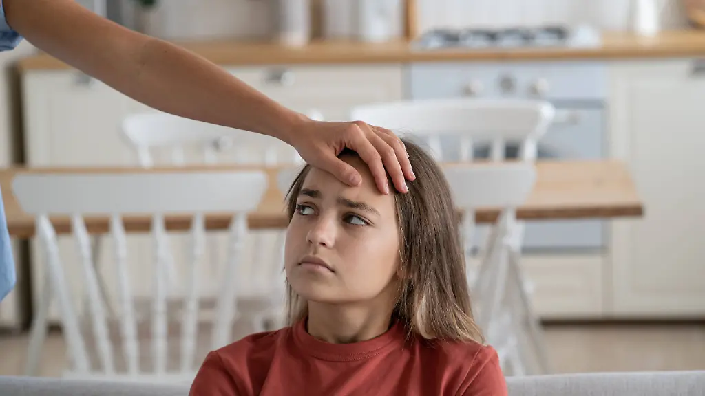 Mother-touching-forehead-of-sick-little-girl-sitting-on-sofa-at-home-checking-temperature-Mother-touching-forehead-of-sick-little-girl-at-home-parent-checking-childs-temperature-without-thermometer-selective-focus-Unhappy-kid-with-fever-feeling-unwell-sitting-on-sofa-looking-at-mom-model-released-Symbolfoto-Copyright-xZoonar