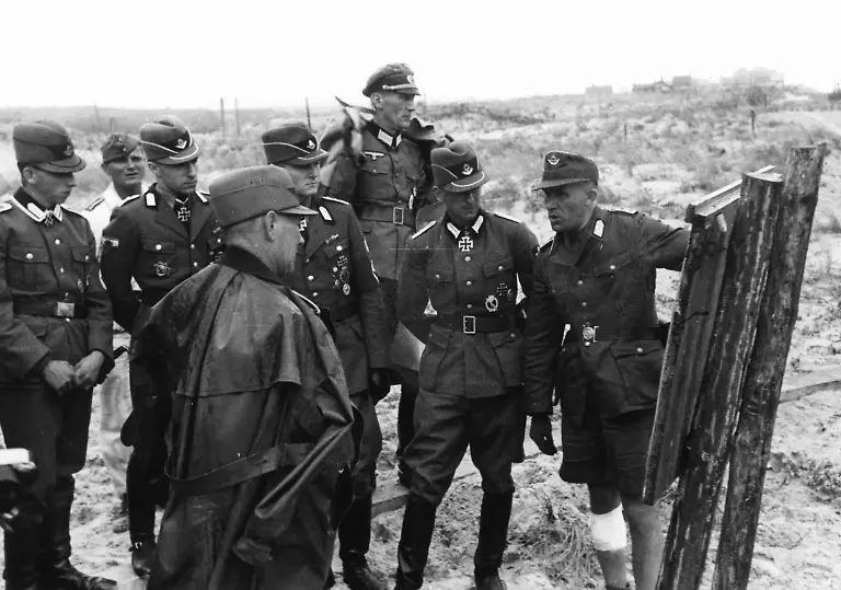 Offiziere-des-Reichsarbeitsdiensts-werden-in-den-Stellungsbau-am-Atlantikwall-eingewiesen-Drei-von-ihnen-sind-Traeger-des-Ritterkreuzes-und-informieren-sich-ueber-die-Arbeiten-an-der-Verteidigungslinie-In-der-Mitte-hinten-ein-Offizier-der-Wehrmacht-Foto-Kreten-Aufnahmedatum-01-01-1943-31-12