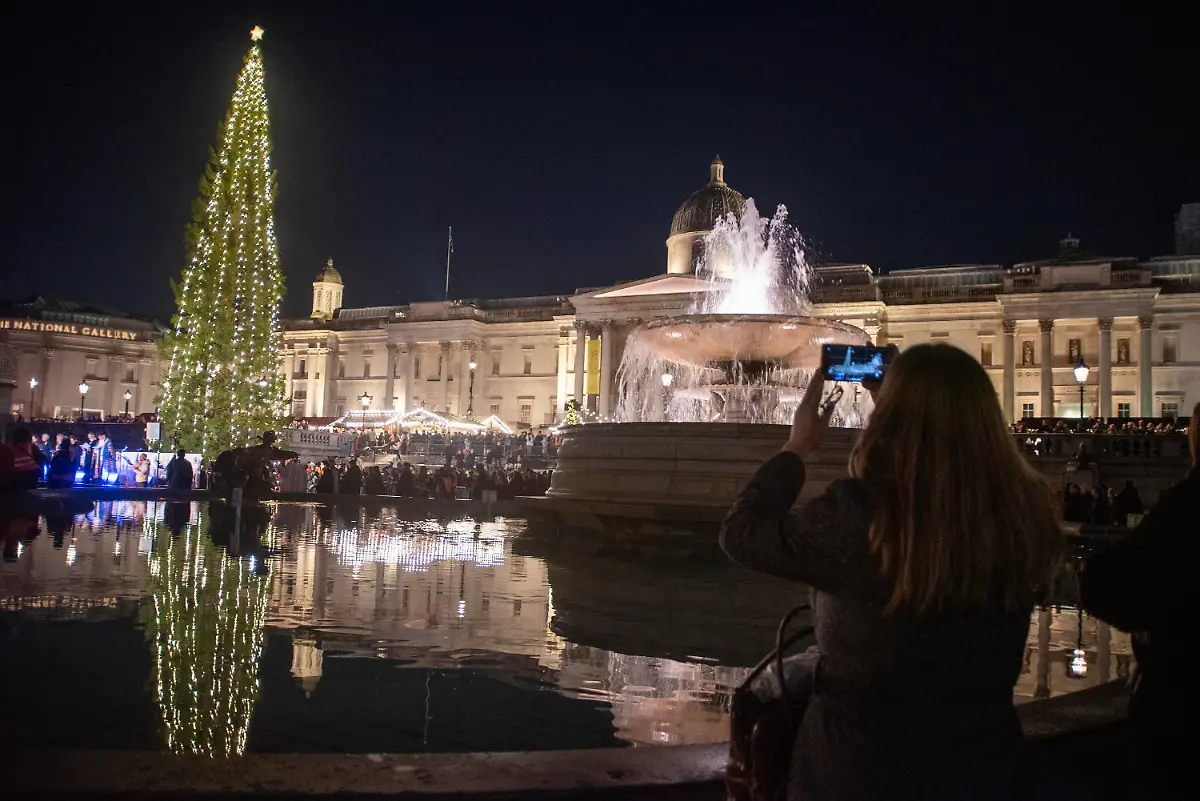 A-spectator-take-a-photo-from-the-fountain-and-the-Christmas-tree-on-the-Trafalgar-Square-in-London-The-Trafalgar-Square-Christmas-tree-is-gift-from-Oslo-Norway-to-UK-to-thank-you-for-the-support-during-the-WWII-The-tradition-started-in-1947-and-the-Norwegian-spruce-has-been-sent-to-London-each-year-to-symbolize-the-strong-relationship-between-the-two-countries