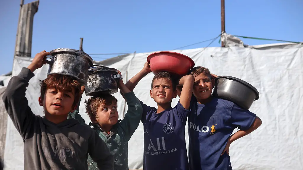 Displaced-Palestinian-children-carry-the-food-containers-they-receive-from-a-charity-kitchen-in-a-displacement-camp-inside-Gaza-Port-on-November-19-2025