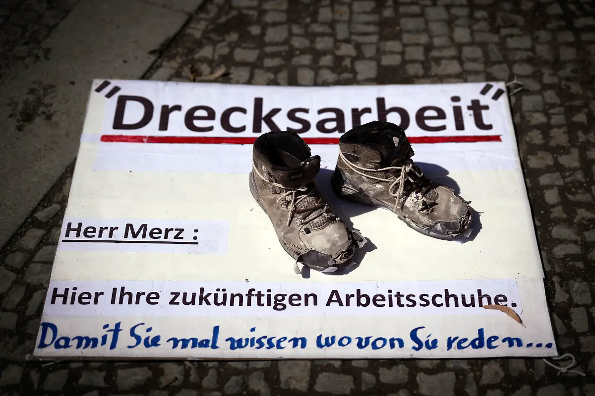 DEU-Deutschland-Germany-Berlin-02-08-2025-Plakat-Drecksarbeit-Herr-Merz-Hier-ihre-zukuenftigen-Arbeitsschuhe-als-Symbol-gegen-die-Politik-vom-Bundeskanzler-Friedrich-Merz-CDU-auf-der-Kundgebung-und-Demonstration-von-der-Querdenker-Bewegung-der-Initative-Querdenken-30-Wir-Sind-Viele-sowie-den-rechten-und-Parteien-wie-AfD-Die-Basis-Die-Heimat-Freie-Sachsen-Gruppe-Deutsche-Jugend-voran-Compact-Verlag-und-rechtsextremen-Gruppen-unter-dem-Motto-Gemeinsam-fuer-den-Weltfrieden-fuer-ein-Leben-in-Frieden-und-Freiheit-und-Wir-sind-das-Volk-vor-dem-Brandenburger-Tor-in-Berlin-Deutschland-Der-Protest-ist-fuer-ein-Stop-von-Waffenlieferungen-an-die-Ukraine-fuer-Volksabstimmungen-und-gegen-die-ehe-staatlichen-Massnahmen-gegen-die-Corona-Pandemie-Zu-den-Demonstratne-gehoeren-Impfgegner-Verschwoerungstheoretiker-und-rechte-Aktivisten-en-Poster-Dirty-Work-Mr-Merz-Here-are-your-future-work-shoes-as-a-symbol-against-the-politics-of-Chancellor-Friedrich-Merz-at-the-rally-and-demonstration-by-the-Querdenker-movement-the-initiative-Querdenken-30-Wir-sind-viele-as-well-as-the-right-wing-parties-such-as-AfD-Die-Basis-Die-Heimat-Freie-Sachsen-Gruppe-Deutsche-Jugend-voran-Compact-Verlag-and-right-wing-extremist-groups-under-the-motto-Together-for-world-peace-for-a-life-in-peace-and-freedom-Weltfrieden-fuer-ein-Leben-in-Frieden-und-Freiheit-and-We-are-the-people-in-front-of-the-Brandenburg-Gate-in-Berlin-Germany-The-protest-is-for-a-stop-to-arms-deliveries-to-Ukraine-for-referendums-and-against-the-former-state-measures-against-the-Corona-pandemic