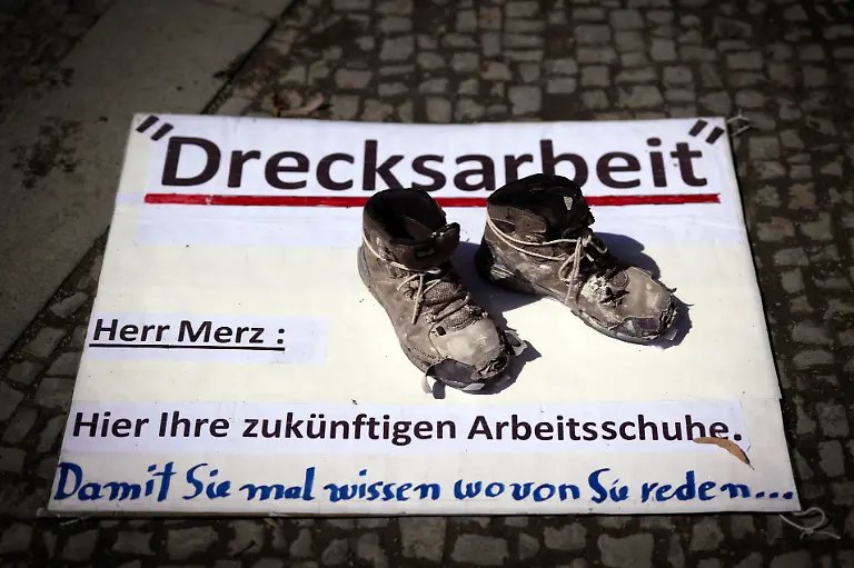 DEU-Deutschland-Germany-Berlin-02-08-2025-Plakat-Drecksarbeit-Herr-Merz-Hier-ihre-zukuenftigen-Arbeitsschuhe-als-Symbol-gegen-die-Politik-vom-Bundeskanzler-Friedrich-Merz-CDU-auf-der-Kundgebung-und-Demonstration-von-der-Querdenker-Bewegung-der-Initative-Querdenken-30-Wir-Sind-Viele-sowie-den-rechten-und-Parteien-wie-AfD-Die-Basis-Die-Heimat-Freie-Sachsen-Gruppe-Deutsche-Jugend-voran-Compact-Verlag-und-rechtsextremen-Gruppen-unter-dem-Motto-Gemeinsam-fuer-den-Weltfrieden-fuer-ein-Leben-in-Frieden-und-Freiheit-und-Wir-sind-das-Volk-vor-dem-Brandenburger-Tor-in-Berlin-Deutschland-Der-Protest-ist-fuer-ein-Stop-von-Waffenlieferungen-an-die-Ukraine-fuer-Volksabstimmungen-und-gegen-die-ehe-staatlichen-Massnahmen-gegen-die-Corona-Pandemie-Zu-den-Demonstratne-gehoeren-Impfgegner-Verschwoerungstheoretiker-und-rechte-Aktivisten-en-Poster-Dirty-Work-Mr-Merz-Here-are-your-future-work-shoes-as-a-symbol-against-the-politics-of-Chancellor-Friedrich-Merz-at-the-rally-and-demonstration-by-the-Querdenker-movement-the-initiative-Querdenken-30-Wir-sind-viele-as-well-as-the-right-wing-parties-such-as-AfD-Die-Basis-Die-Heimat-Freie-Sachsen-Gruppe-Deutsche-Jugend-voran-Compact-Verlag-and-right-wing-extremist-groups-under-the-motto-Together-for-world-peace-for-a-life-in-peace-and-freedom-Weltfrieden-fuer-ein-Leben-in-Frieden-und-Freiheit-and-We-are-the-people-in-front-of-the-Brandenburg-Gate-in-Berlin-Germany-The-protest-is-for-a-stop-to-arms-deliveries-to-Ukraine-for-referendums-and-against-the-former-state-measures-against-the-Corona-pandemic