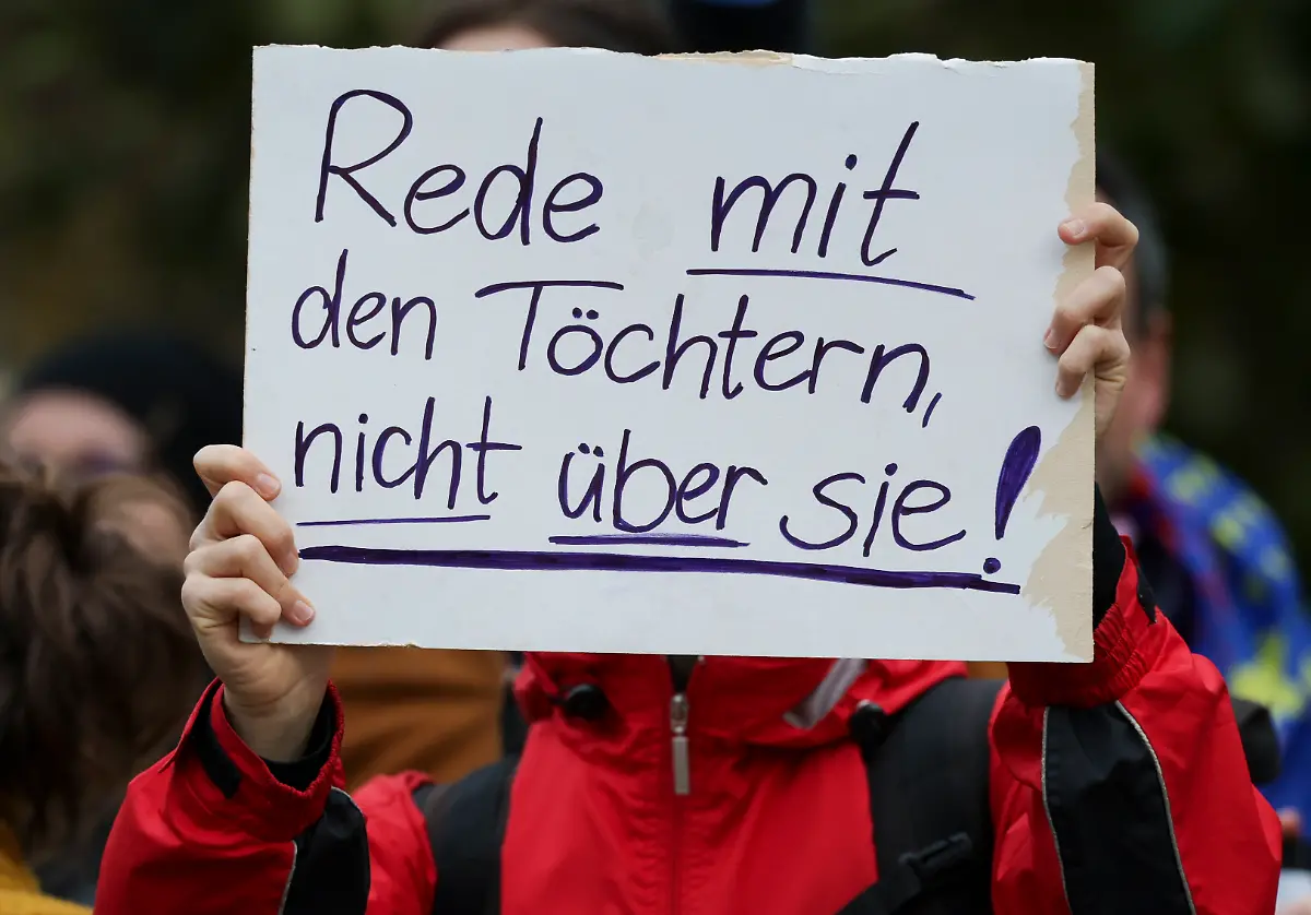 Eine-Demonstrantin-protestiert-mit-einem-Schild-mit-der-Aufschrit-Rede-mit-den-Toechtern-nicht-ueber-sie-gegen-des-Stadtbild-Zitat-waehrend-des-Antrittsbesuchs-gegen-Bundeskanzler-Merz-vor-der-saechsischen-Staatskanzlei