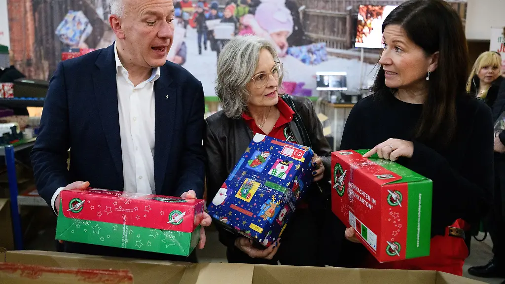Berlins-Regierender-Buergermeister-Kai-Wegner-und-Bildungssenatorin-Katharina-Guenther-Wuensch-ganz-rechts-machen-sich-ein-Bild-von-der-Aktion-Weihnachten-im-Schuhkarton