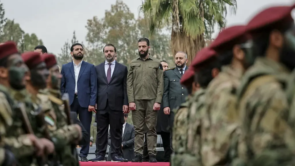 This-handout-photograph-released-by-the-official-Syrian-Arab-News-Agency-SANA-on-December-8-2025-shows-Syria-s-President-Ahmed-al-Sharaa-CR-and-Syrian-Minister-of-Foreign-Affairs-and-Expatriates-Asaad-Al-Shaibani-CL-observing-the-military-parade-in-Damascus-during-the-anniversary-of-the-ousting-of-longtime-ruler-Bashar-al-Assad-President-Ahmed-al-Sharaa-on-December-8-urged-Syrians-to-work-together-to-rebuild-their-country-as-they-marked-a-year-since-the-ousting-of-longtime-ruler-Bashar-al-Assad-Sharaa-s-Islamist-led-alliance-launched-a-lightning-offensive-in-late-November-last-year-taking-the-capital-Damascus-on-December-8-after-nearly-14-years-of-war-and-putting-an-end-to-more-than-five-decades-of-the-Assad-family-s-iron-fisted-rule