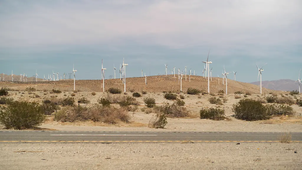 Wind-turbines-dot-a-dry-desert-landscape-under-a-wide-pale-sky