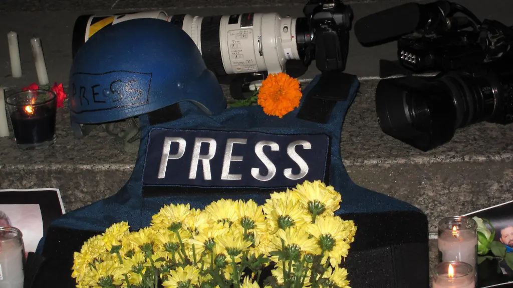 Ein-Helm-Kameras-und-eine-Schutzweste-Ausruestungsgegenstaende-von-Journalisten-die-in-Kriegsgebieten-arbeiten-liegen-bei-einer-Mahnwache-neben-Blumen-und-Kerzen-auf-dem-Foley-Square-67-Journalistinnen-und-Journalisten-sind-in-den-zurueckliegenden-12-Monaten-weltweit-im-Zusammenhang-mit-ihrer-Arbeit-getoetet-worden
