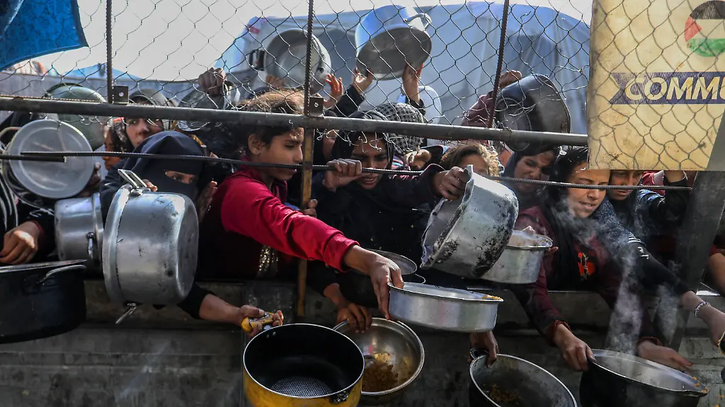 KHAN-YUNIS-GAZA-DECEMBER-8-Palestinians-line-up-with-their-containers-in-hand-to-receive-hot-meals-distributed-by-aid-organizations-in-Mawasi-as-the-food-crisis-deepened-after-IsraelAeos-attacks-in-Khan-Yunis-Gaza-on-June-15-2025