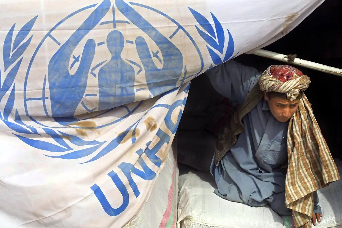 Ein-afghanischer-Fluechtling-entlaedt-am-23-11-2001-Hilfsgueter-die-vom-UN-Fluechtlingshilfswerkes-UNHCR-und-vom-iranischen-Roten-Halbmond-in-das-Fluechtlingslager-Minarah-vor-der-westafghanischen-Stadt-Herat-gebracht-worden-sind-Die-Lastwagen-drei-vom-UNHCR-und-12-vom-Roten-Halbmond-kamen-mit-12000-Plastikdecken-10000-Decken-und-Lebensmitteln-fuer-mehr-als-12000-Menschen-aus-dem-Iran-Allein-bei-Herat-sind-in-einem-Lager-200000-Obdachlose-untergebracht-worden-Im-Wettlauf-gegen-den-bevorstehenden-Einbruch-des-Winters-wollen-die-internationalen-Hilfsorganisationen-ihre-Aktivitaeten-in-Afghanistan-weiter-verstaerken-Die-Sicherheitslage-wird-von-den-Hilfsorganisationen-weiterhin-als-sehr-schwierig-beschrieben