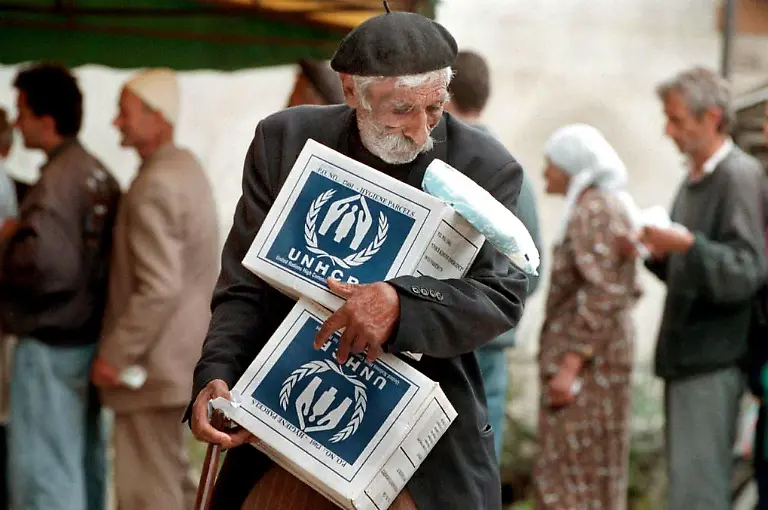 Ein-aelterer-Albanier-traegt-am-25-6-1999-in-Pec-zwei-UNHCR-Hilfspakete-mit-Nahrungsmitteln-fort-die-er-in-einer-Ausgabestelle-des-UN-Fluechtlingshilfswerkes-erhalten-hat-Pec-gehoert-zu-den-Staedten-im-Kosovo-deren-120000-Bewohner-durch-den-Buergerkrieg-stark-gelitten-haben-Zudem-steigt-mit-der-rasanten-Rueckkehr-der-Vertriebenen-in-das-Kosovo-die-Zahl-der-Fluechtlinge-ohne-Obdach-Rund-40-Prozent-der-Haeuser-wurden-beschaedigt-oder-zerstoert-so-ein-Sprecher-des-UNHCR-am-29-6-1999-in-Pristina-Tausende-leben-in-Notunterkuenften