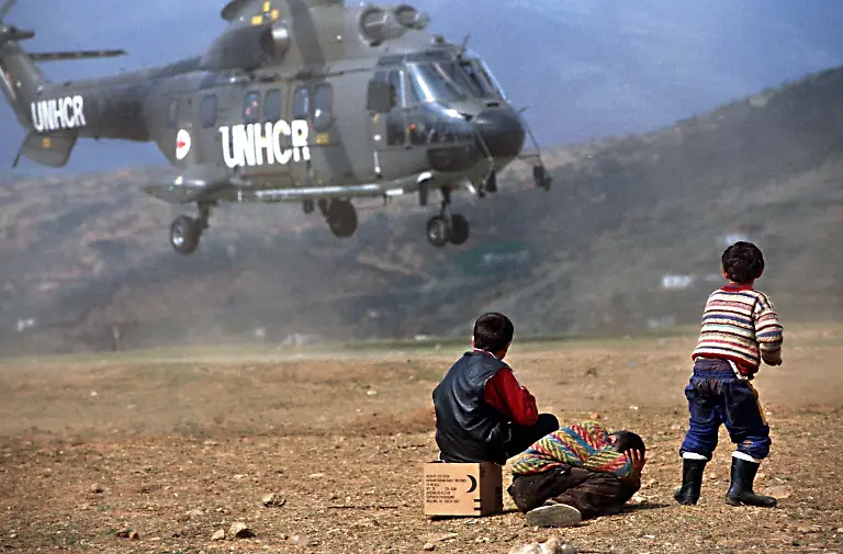 Drei-Fluechtlingskinder-aus-dem-Kosovo-beobachten-am-17-April-1999-im-Fluechtlingslager-in-Kukes-in-Albanien-einen-Hubschrauber-des-UNHCR-des-Fluechtlingshilfswerkes-der-Vereinten-Nationen-der-zur-Landung-ansetzt