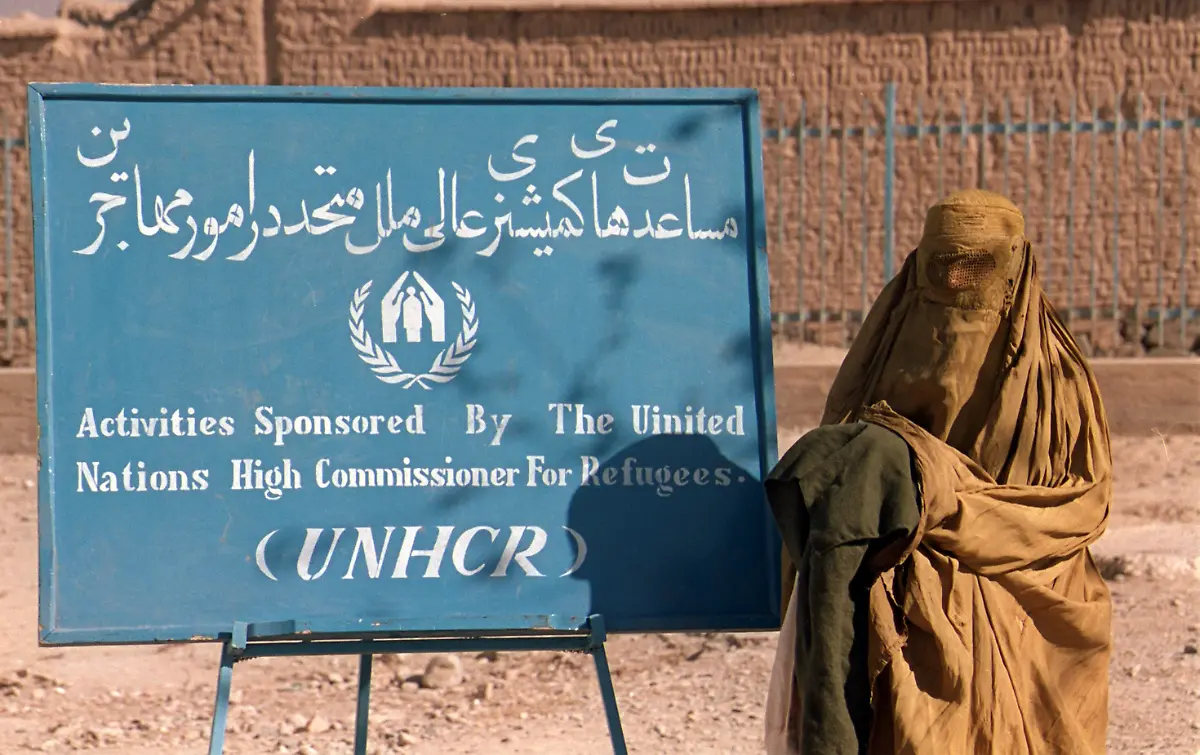 Eine-tiefverschleierte-Frau-geht-am-12-11-1996-in-Kabul-an-einem-Plakat-der-UN-Fluechtlingshilfswerks-UNHCR-vorbei-zu-einer-Ausgabestelle-fuer-Handtuecher-und-warme-Kleidung-Die-UN-Organisation-verteilt-hier-vor-dem-kommenden-Winter-an-Beduerftige-Hilfspakate-Afghanische-Frauen-duerfen-sich-seit-der-Einnahme-Kabuls-durch-die-radikal-islamische-Taliban-Milizen-nur-noch-verschleiert-in-der-Oeffentlichkeit-zeigen