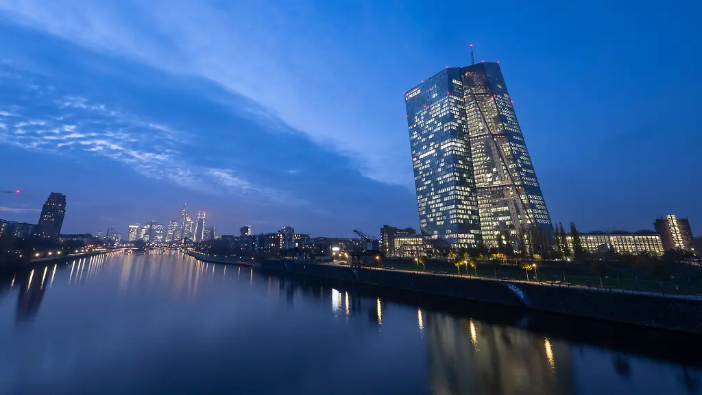 Die-Lichter-in-den-Bueros-der-Europaeischen-Zentralbank-leuchten-im-letzten-Tageslicht-waehrend-sich-die-Skyline-im-Main-spiegelt