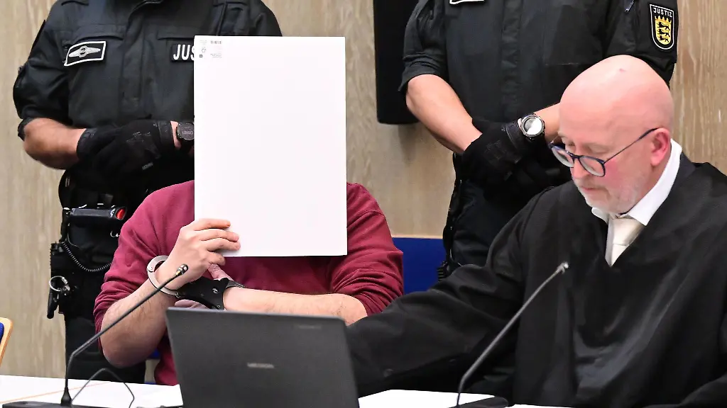 Der-Angeklagte-in-einem-Mordprozess-nach-einer-Todesfahrt-von-Mannheim-sitzt-mit-einem-Aktendeckel-vor-seinem-Gesicht-im-Gerichtssaal-rechts-neben-ihm-sitzt-sein-Verteidiger-Uwe-Kosmala