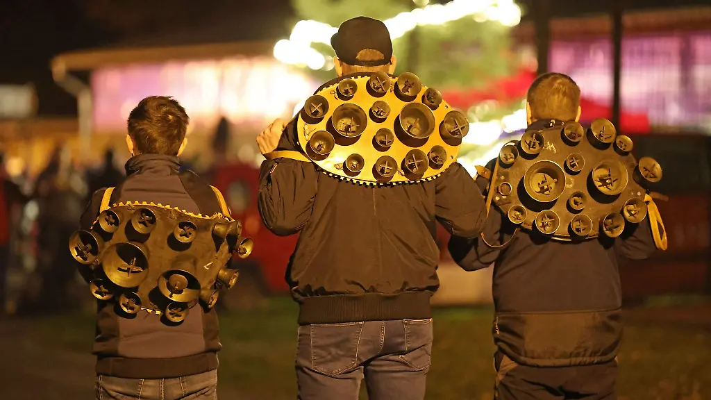 Drei-Mitglieder-der-Brauchtumsgruppe-Weihnachtsmaenner-e-V-stehen-mit-Schellengelaeut-auf-dem-Weihnachtsmarkt-in-Altenbrak-Am-ersten-Feiertag-ziehen-sie-in-kompletter-Dunkelheit-durch-den-Ort