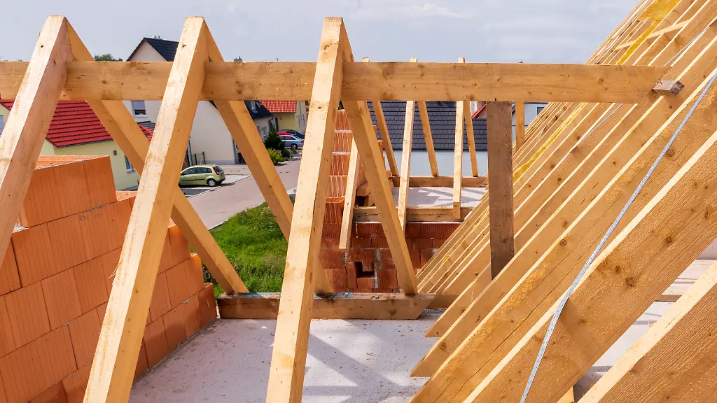 Auf-dem-Neubau-von-einem-Wohnhaus-wird-mit-Dachbalken-ein-neuer-Dachstuhl-montiert-als-Symbolbild-fuer-Wohnbau-und-Wohnungspolitik