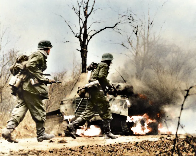 World-War-II-Battle-of-the-Bulge-Ardennes-Offensive-last-major-German-offensive-campaign-on-the-Western-Front-December-1944-January-1945-German-troops-advancing-past-burning-American-equipment-Belgium-Photo-taken-from-captured-German-film-1944-45