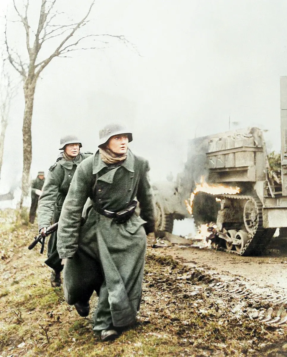 World-War-II-Battle-of-the-Bulge-Ardennes-Offensive-last-major-German-offensive-campaign-on-the-Western-Front-December-1944-January-1945-German-infantry-advancing-during-the-Battle-of-the-Bulge-two-soldiers-pass-a-burning-US-Army-vehicle-Photo-1944