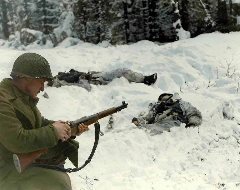 World-War-II-Battle-of-the-Bulge-Ardennes-Offensive-last-major-German-offensive-campaign-on-the-Western-Front-December-1944-January-1945-Pfc-Frank-Vukasin-Great-Falls-Mont-stops-to-load-clip-in-rifle-while-advancing-in-snow-covered-front-line-sector-at-Houffalize-Belgium-Two-dead-Germans-are-wearing-camouflaged-snow-uniforms-Company-C-331st-Infantry-Regiment-83rd-Infantry-Division-Photo-1944-45