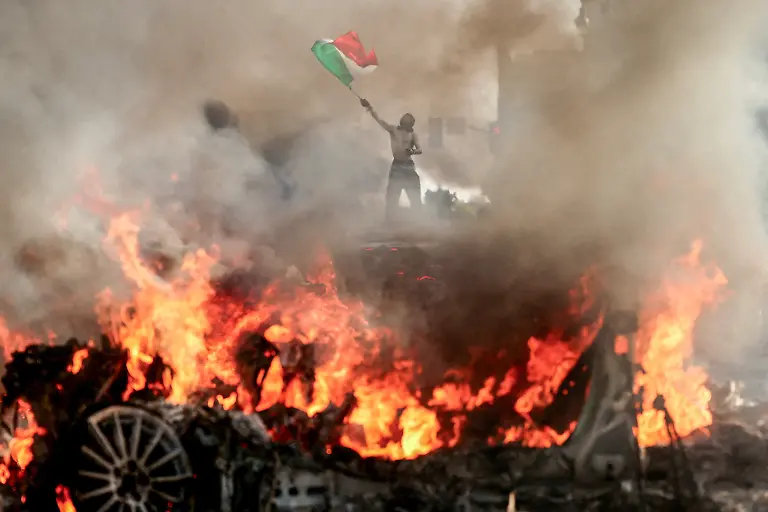 A-man-waves-a-Mexican-flag-as-smoke-and-flames-rise-from-a-burning-vehicle-during-a-protest-against-federal-immigration-sweeps-near-Los-Angeles-City-Hall-in-downtown-Los-Angeles-California-U-S-June-8-2025-REUTERS-David-Swanson-TPX-IMAGES-OF-THE-DAY-SEARCH-REUTERS-BEST-2025-FOR-THIS-STORY-SEARCH-REUTERS-2025-YEAR-END-FOR-ALL-2025-YEAR-END-GALLERIES