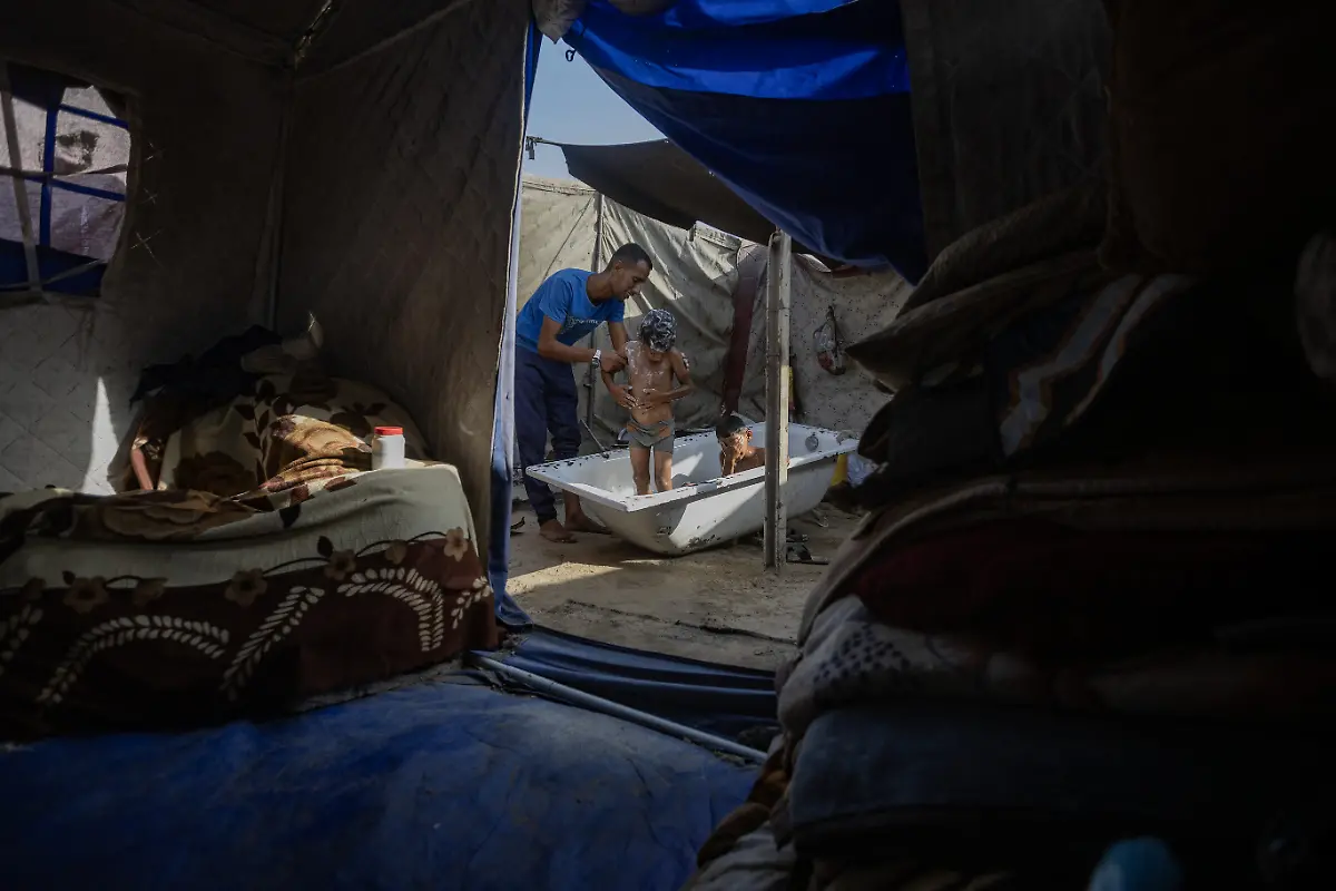 NYTCEASEFIRE-August-15-2025-Gaza-City-Displaced-children-fill-a-large-container-of-water-inside-their-tent-taking-a-shower-to-escape-the-high-temperatures