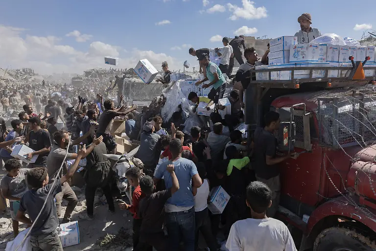 NYTCEASEFIRE-October-12-2025-Khan-Yunis-Hundreds-of-Palestinians-run-toward-aid-trucks-after-they-entered-through-the-Kerem-Shalom-crossing-passing-through-the-Morag-axis-separating-Rafah-and-Khan-Yunis