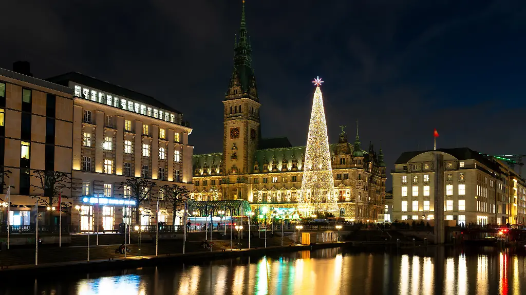 Vor-dem-Hamburger-Rathaus-erstrahlt-der-grosse-Weihnachtsbaum-und-taucht-den-Rathausmarkt-in-festliches-Licht-Die-Spiegelungen-auf-dem-Wasser-und-die-historische-Kulisse-praegen-die-winterliche-Atmosphaere-der-Innenstadt
