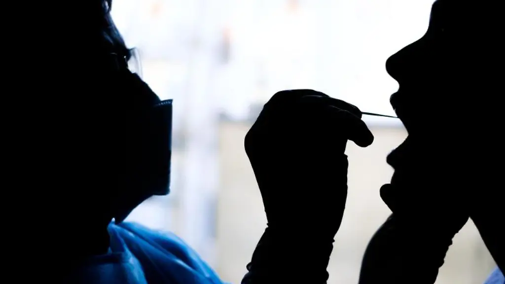 Ein-Facharzt-fuer-Allgemeinmedizin-nimmt-bei-einer-Patientin-einen-Rachenabstrich-fuer-einen-Covid-19-Schnelltest