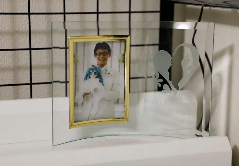 A-framed-wedding-photo-of-Akihiko-Kondo-43-who-married-the-persona-of-Hatsune-Miku-a-virtual-pop-idol-in-2018-sits-on-his-bed-at-his-home-in-Matsudo-Chiba-Prefecture-Japan-February-24-2025-REUTERS-Kim-Kyung-Hoon-SEARCH-JAPAN-KYUNG-HOON-AI-WEDDING-FOR-THIS-STORY-SEARCH-WIDER-IMAGE-FOR-ALL-STORIES