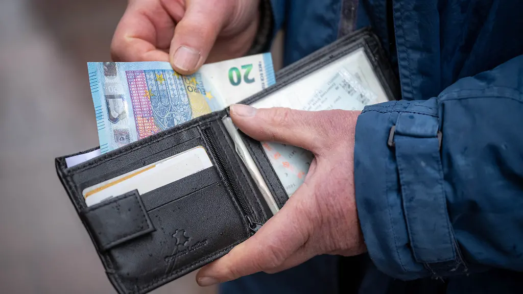 Eine-aeltere-Person-haelt-im-oeffentlichen-Raum-eine-geoeffnete-Geldboerse-in-der-Hand-aus-der-ein-20-Euro-Schein-hervorschaut-Im-Bundestag-steht-am-Freitag-die-Entscheidung-ueber-die-geplante-Rentenreform-an-die-ein-stabiles-Rentenniveau-erweiterte-Kindererziehungszeiten-steuerfreie-Zuverdienstmoeglichkeiten-im-Alter-und-weitere-Aenderungen-in-der-Altersvorsorge-vorsieht