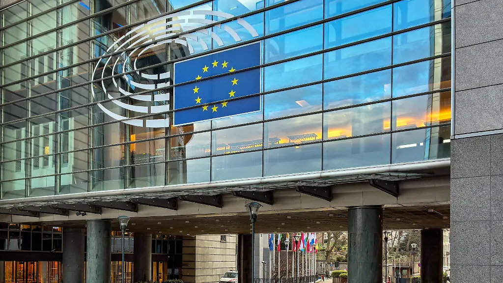 A-large-vinyl-decal-displaying-the-official-circular-logo-of-the-European-Parliament-along-with-the-full-blue-and-yellow-starred-flag-of-the-European-Union-is-affixed-to-the-glass-curtain-wall-of-the-institution-s-building-in-Brussels-Belgium-on-December-16-2025