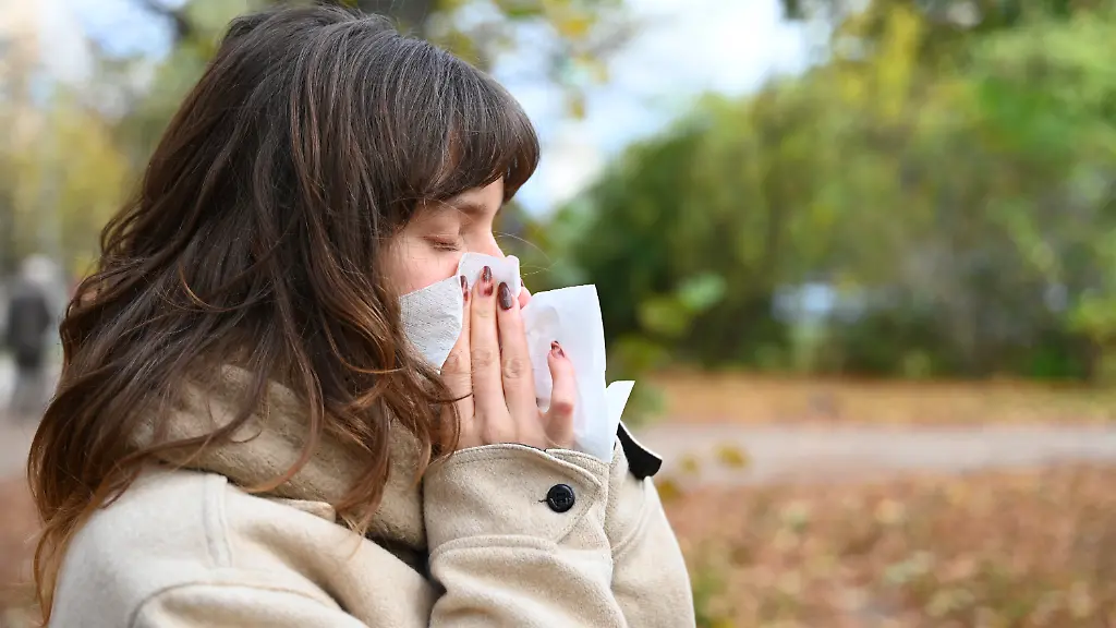 Eine-Frau-putzt-sich-in-einem-Park-mit-einem-Taschentuch-die-Nase-Die-Zahl-akuter-Atemwegserkrankungen-liegt-dem-aktuellen-Wochenbericht-des-Robert-Koch-Instituts-RKI-zufolge-auf-moderatem-Niveau-Hochgerechnet-aus-freiwilligen-Meldungen-der-Bevoelkerung-geht-das-RKI-von-rund-7-500-Erkrankungen-pro-100-000-Einwohner-aus