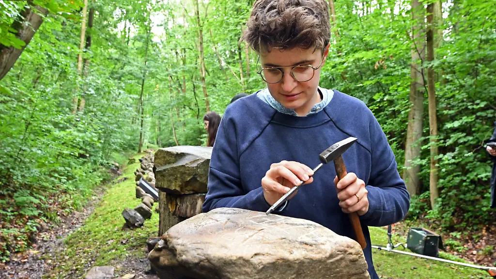 Anna-Nicole-Heinrich-Praeses-der-Synode-der-Evangelischen-Kirche-in-Deutschland-EKD-bearbeitet-einen-Stein-am-Gedenkweg-Buchenwaldbahn-beim-Besuch-im-Bildungscamp-der-Aktion-Suehnezeichen-Friedensdienste-e-V-in-der-Gedenkstaette-Buchenwald-Die-Teilnehmer-unterstuetzen-mit-praktischer-Arbeit-den-Gedenkort-und-lernen-ueber-die-Geschichte-des-ehemaligen-Konzentrationslagers